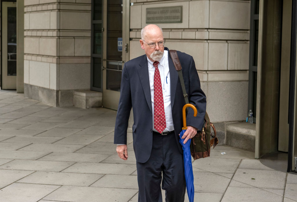 John Durham walking outside a federal courthouse in Washington, D.C., carrying an umbrella and a bag