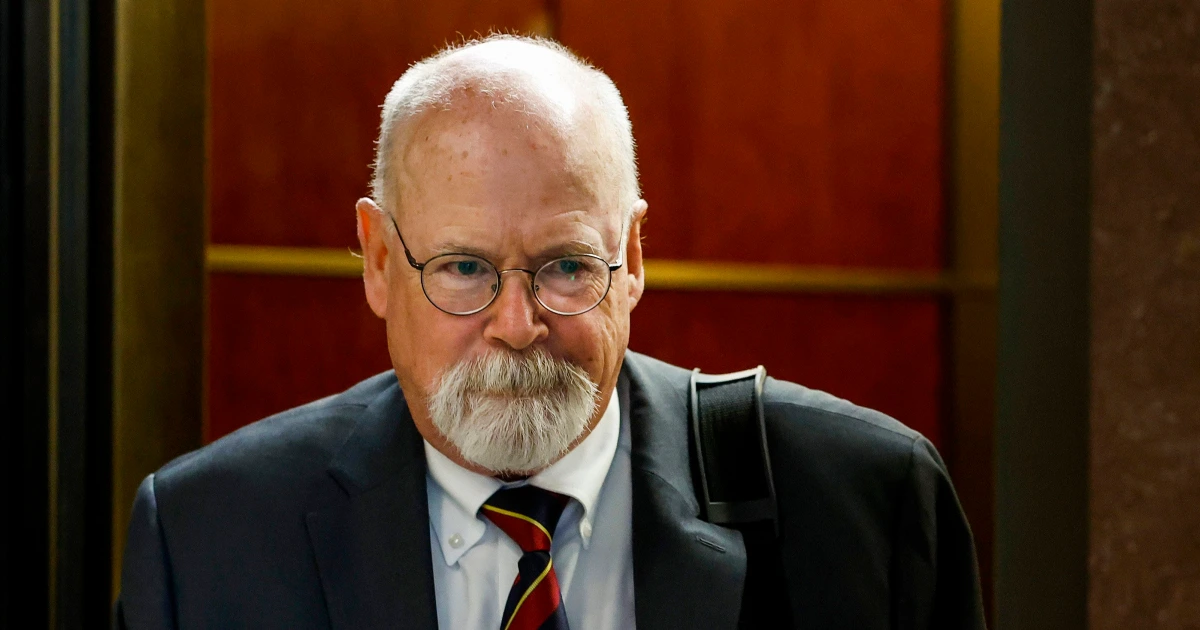 John Durham stepping off an elevator at a federal courthouse, wearing glasses and a tie