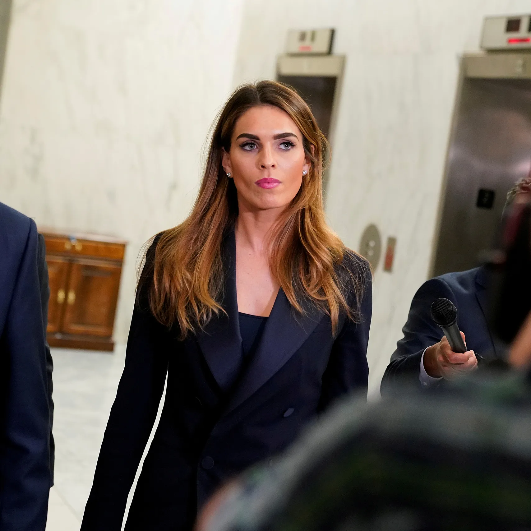 Hope Hicks walking through a Capitol hallway past reporters holding out a microphone