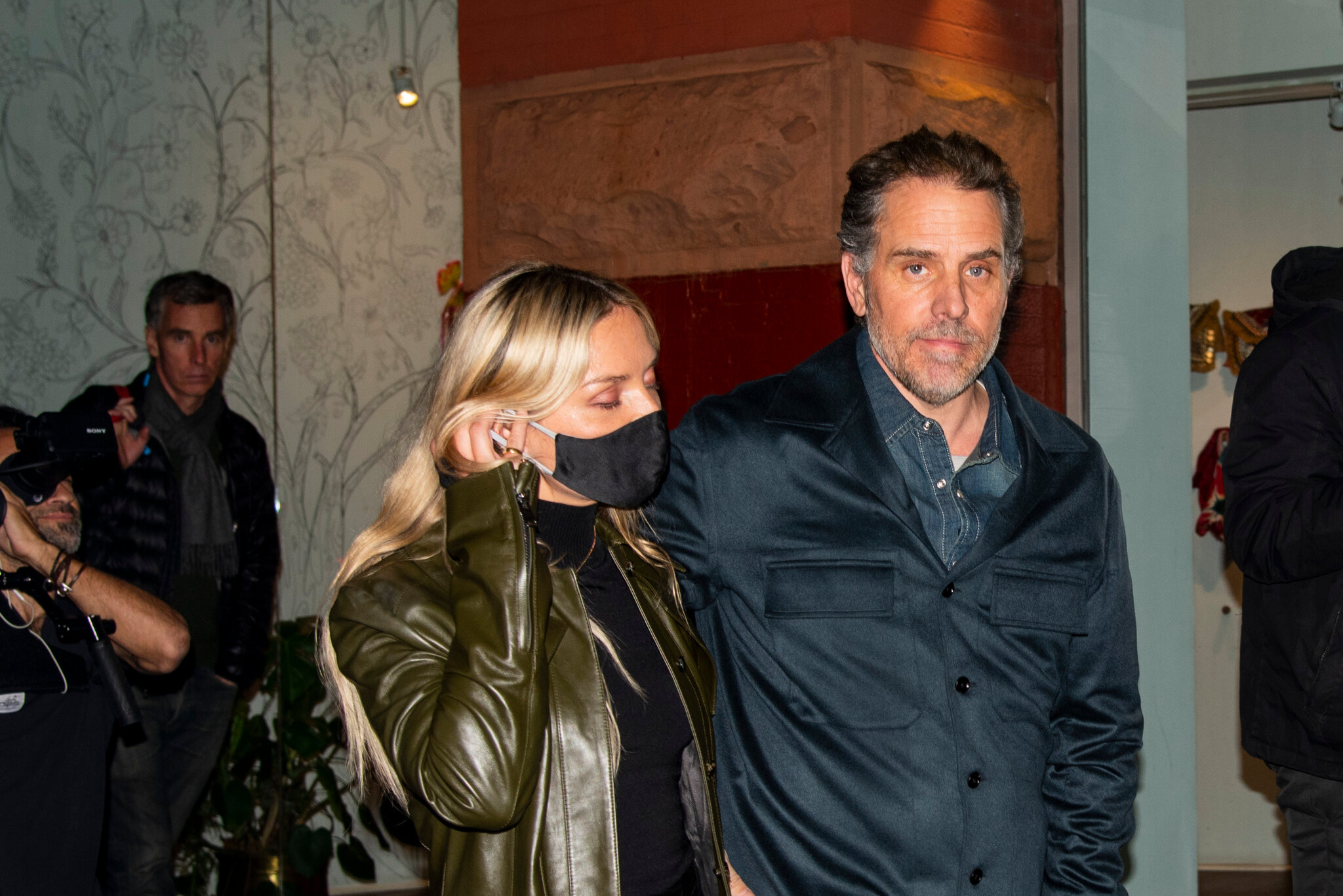 Hunter Biden walking beside a companion wearing a black face mask, flanked by security and photographers