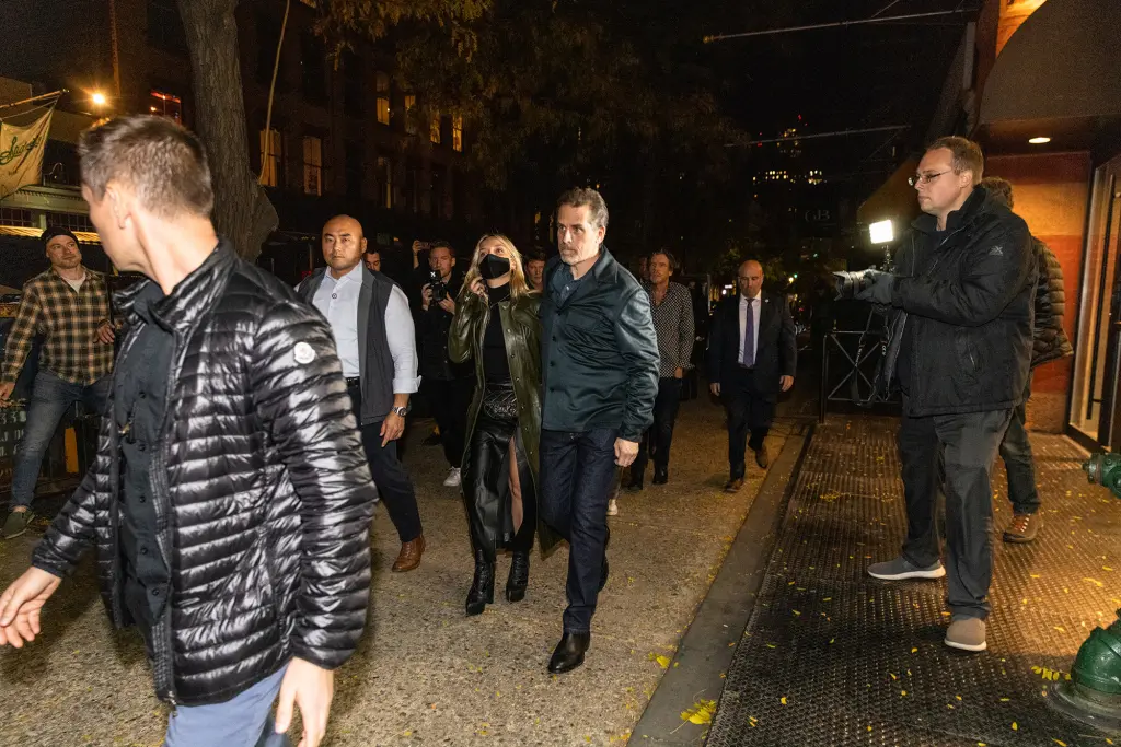 A wider street view of Hunter Biden and his group walking past a crowd of photographers and onlookers at night