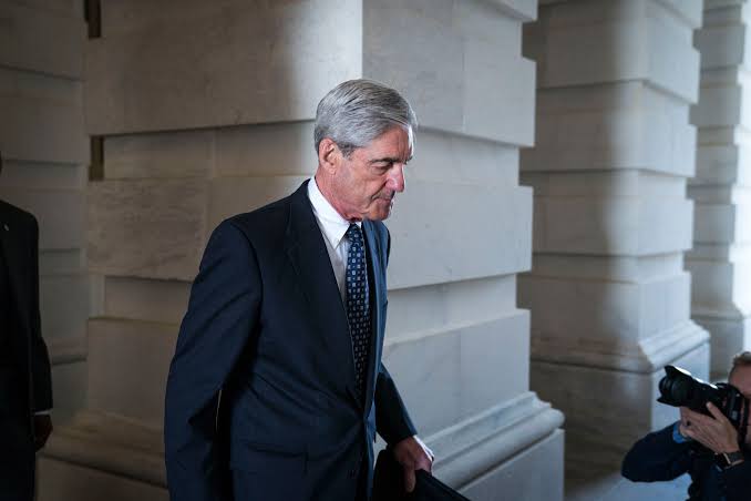 Robert Mueller walking through a corridor at the U.S. Capitol, followed by a photographer