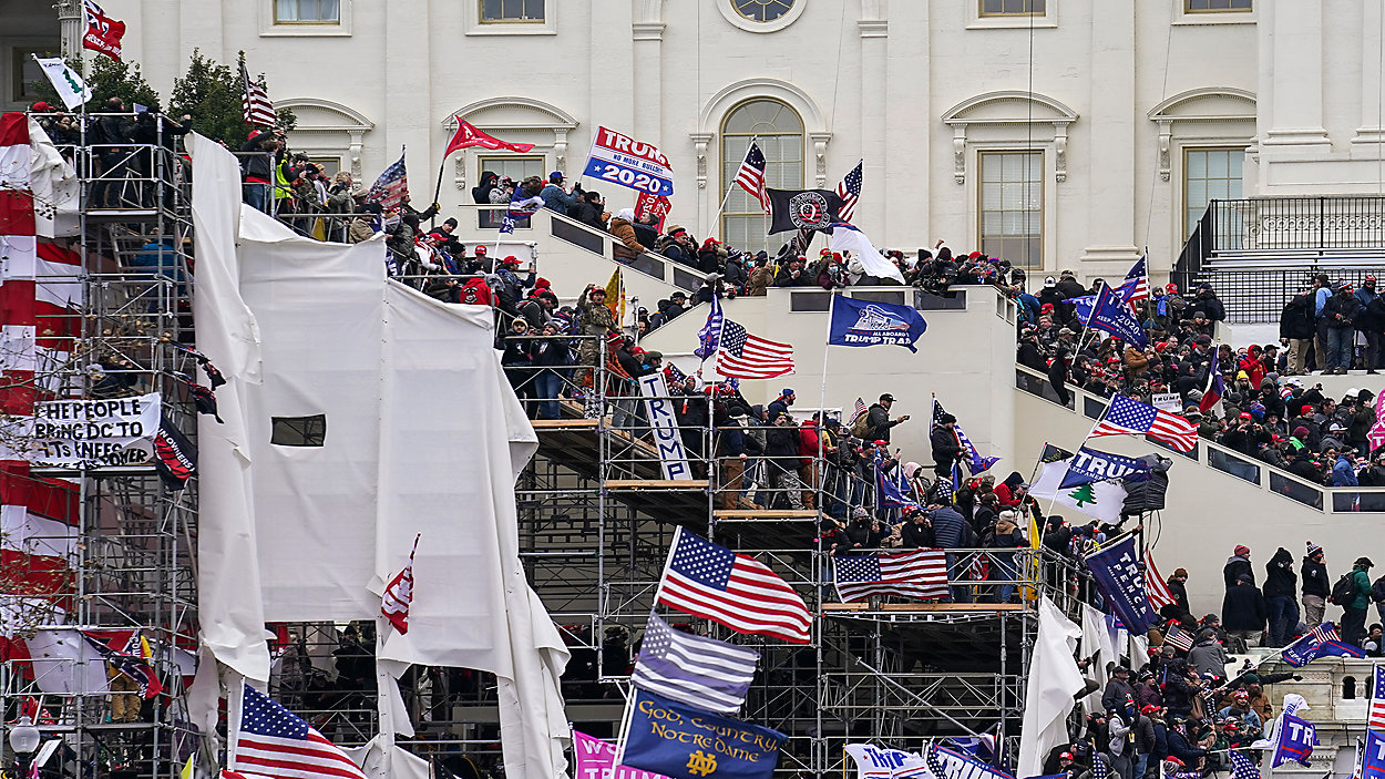 Crowds of Trump supporters on January 6, 2021 climbing the white-shrouded inauguration scaffolding and packing the stairs of the Capitol's West Front, waving American flags, Trump 2020 banners, an Appeal to Heaven flag and a Notre Dame flag