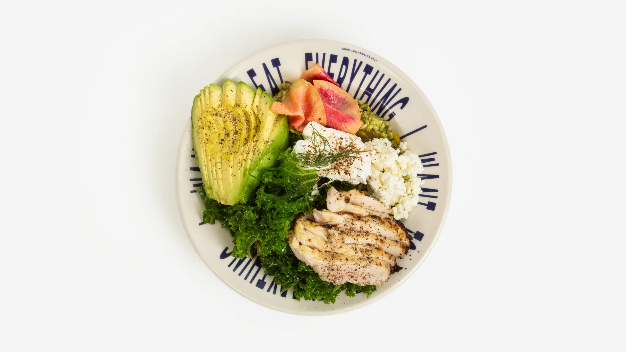 A Sqirl rice bowl with avocado, kale, poached egg, and grilled chicken, served on a plate printed with the words Eat Everything I Want