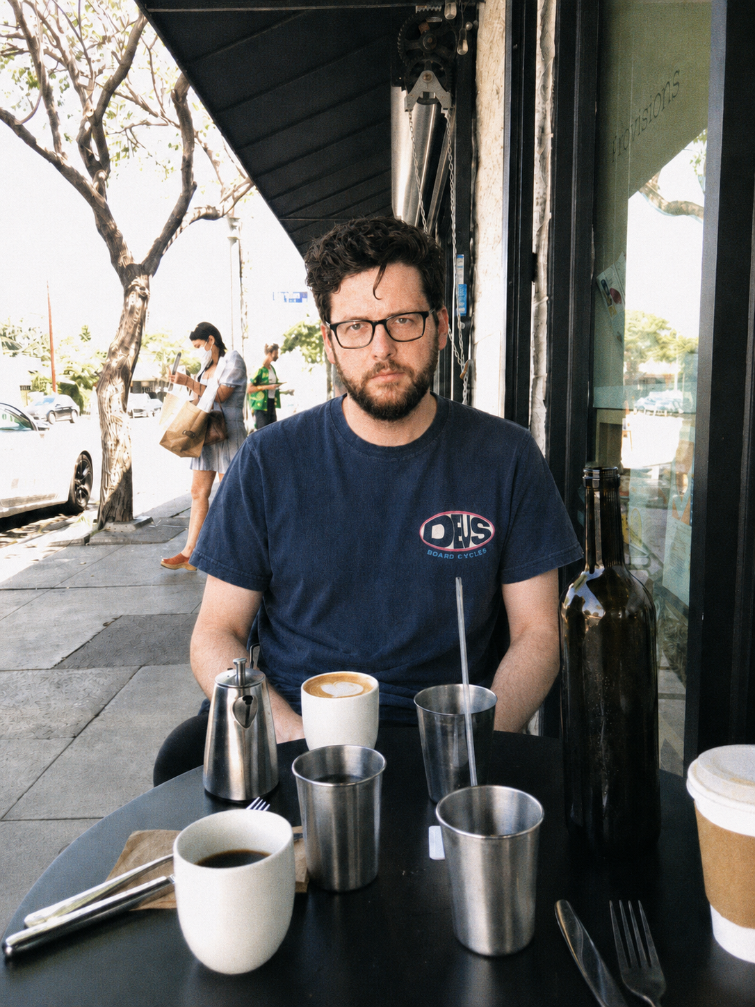 Michael Mendy sitting at an outdoor table at Sqirl in Los Angeles, with coffee, cortados, and an empty wine bottle used as a water carafe