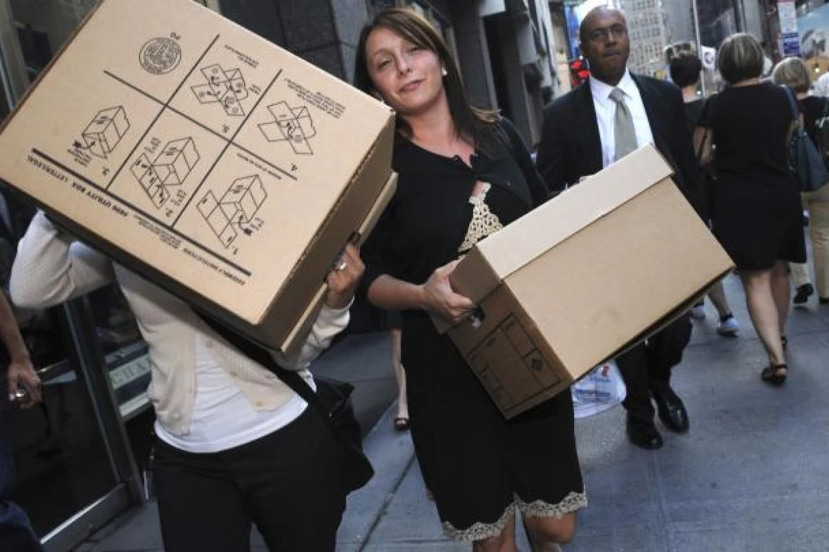 Two Lehman Brothers employees carrying cardboard file boxes along a crowded New York sidewalk on the day the firm filed for bankruptcy, one with a box hoisted on her shoulder