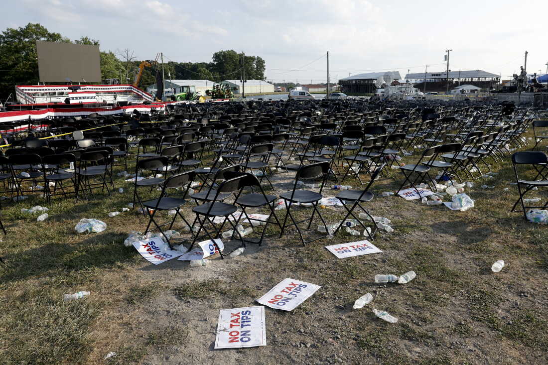 Rows of empty folding chairs on the rally grounds after the evacuation, scattered with dropped water bottles and 'No Tax On Tips' campaign signs, the stage visible in the background