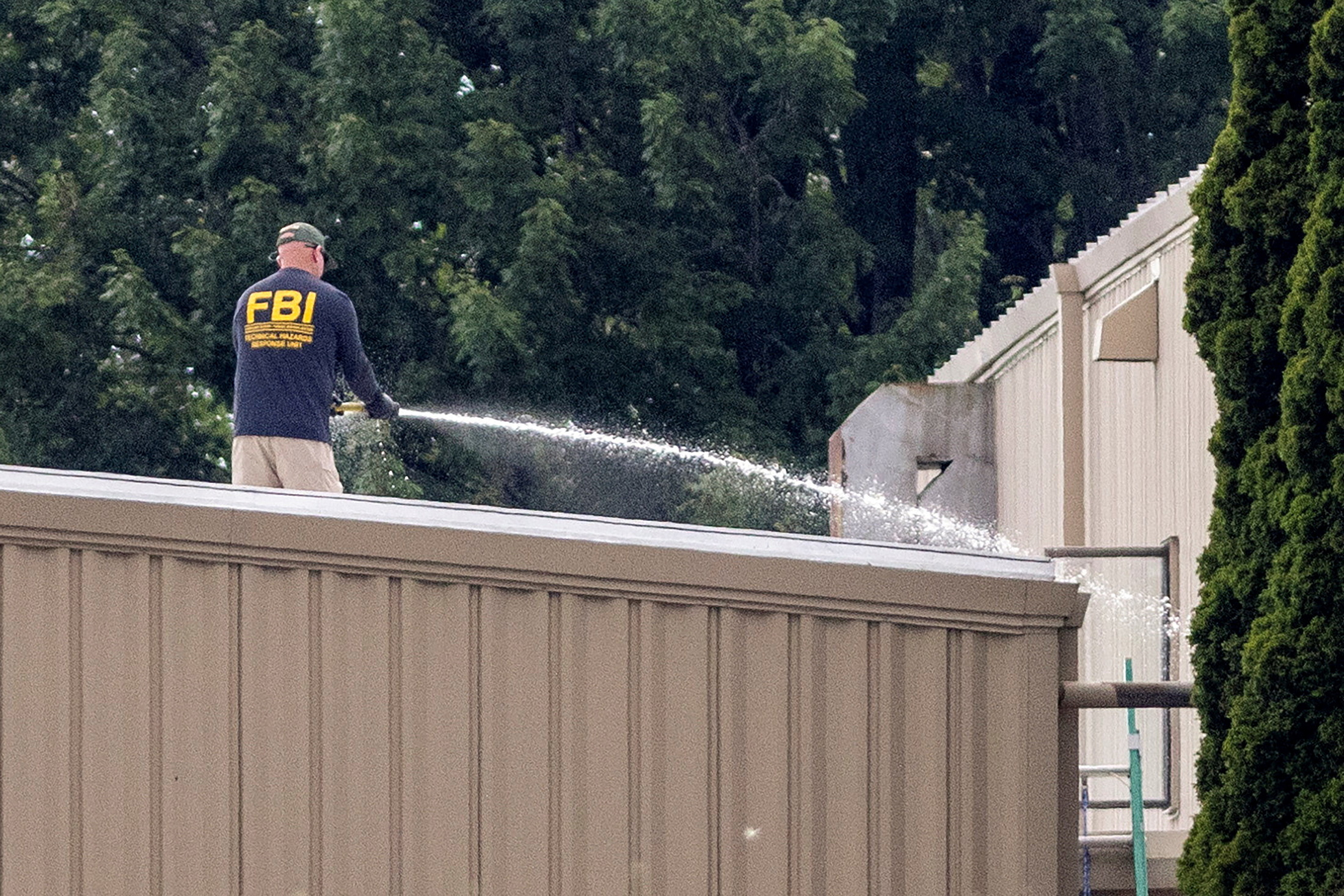 An FBI Technical Hazards Response Unit agent standing on the AGR International rooftop, hosing it down with water as part of the post-shooting evidence and decontamination work