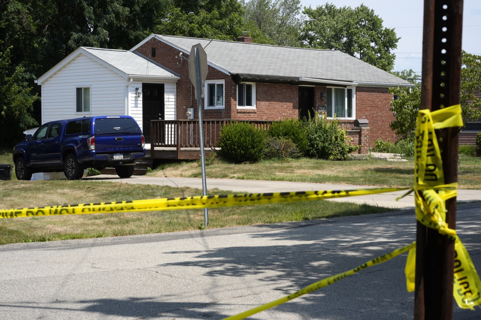 The Crooks family's brick ranch home in Bethel Park, Pennsylvania, cordoned off with yellow police tape strung between a stop sign and a utility pole, a blue pickup truck parked in the driveway
