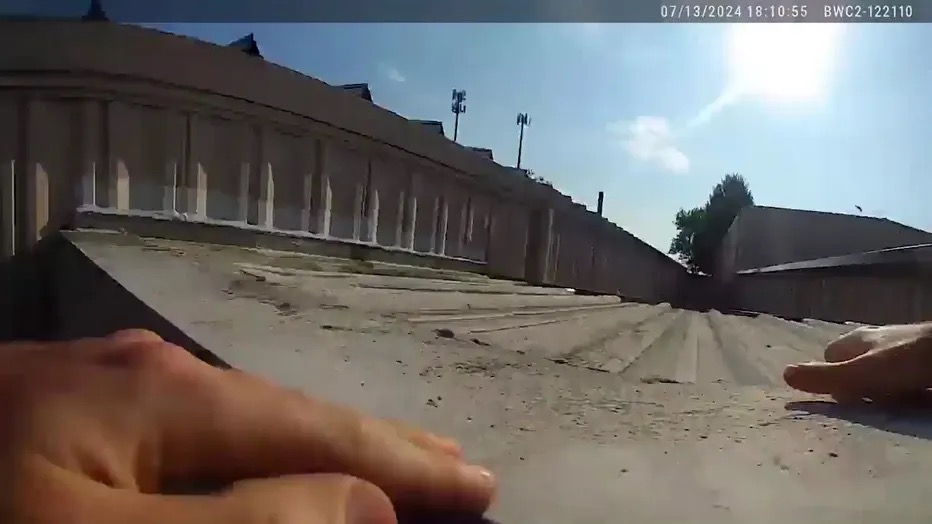 Body camera footage timestamped 07/13/2024 18:10:55, showing an officer's own hands gripping the edge of the AGR International rooftop as he pulls himself up