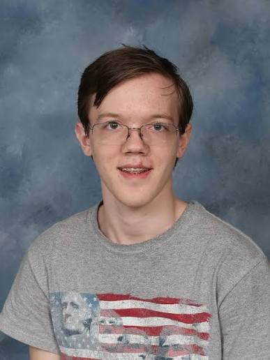 A school portrait of a teenage Thomas Crooks, wearing glasses and braces, in a gray t-shirt printed with an American flag and Mount Rushmore