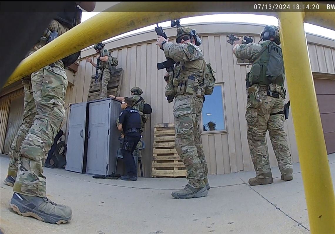 Body camera footage timestamped 07/13/2024 18:14:20, showing a tactical team with rifles raised moving in around the AGR International building alongside a local police officer