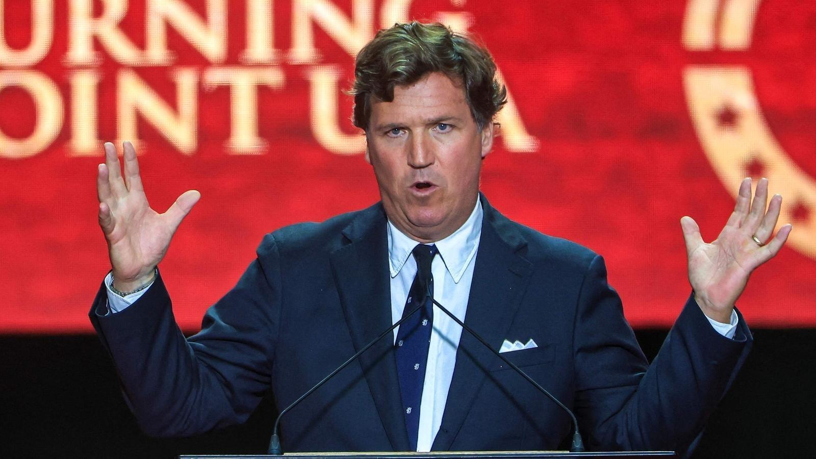 Tucker Carlson speaking at a Turning Point USA event in front of a red backdrop