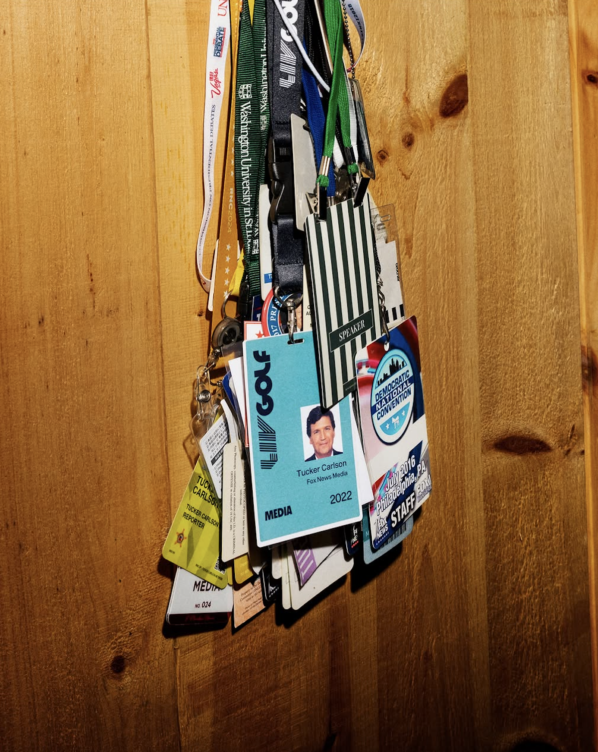 A wall of press lanyards and badges, including a Tucker Carlson Fox News Media badge from 2022 and a Democratic National Convention staff pass from July 2016