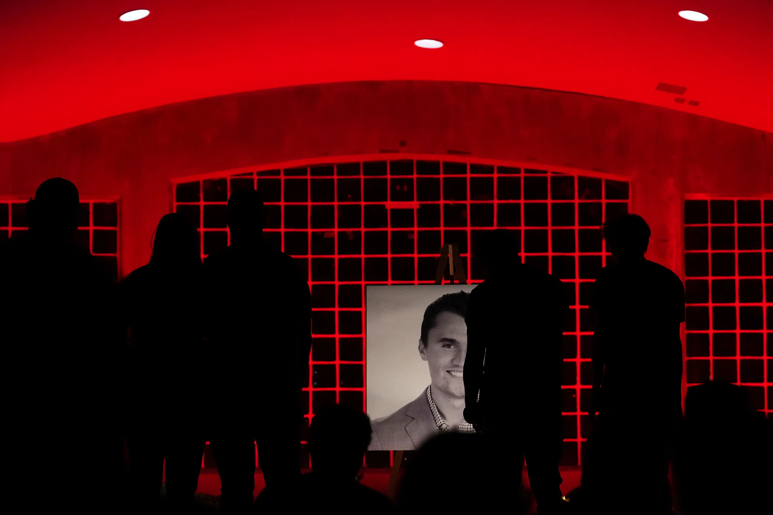 Silhouettes of mourners at a candlelight vigil for Charlie Kirk, hosted by the Young Republicans Club of New York in Madison Square Park, standing before a black-and-white portrait of Kirk on an easel