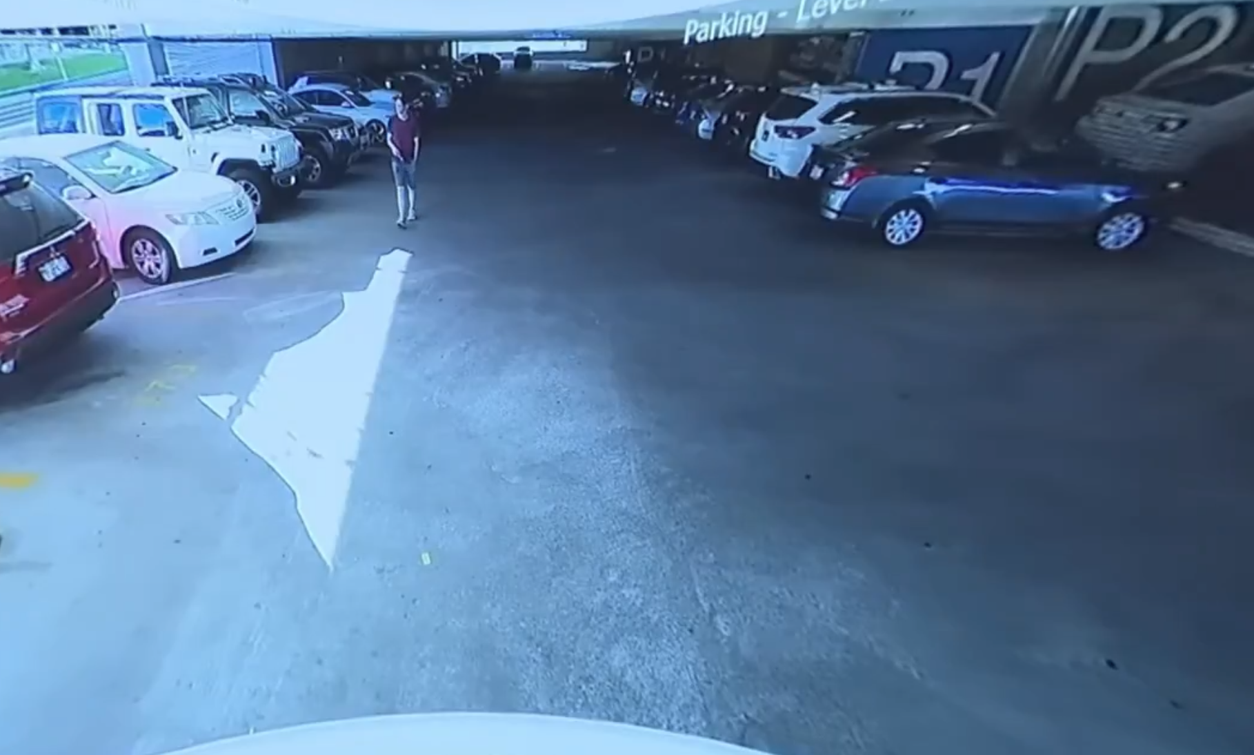 Surveillance still from the Utah Valley University parking garage showing a man in a maroon shirt walking past a row of parked cars, presented at Tyler Robinson's preliminary hearing