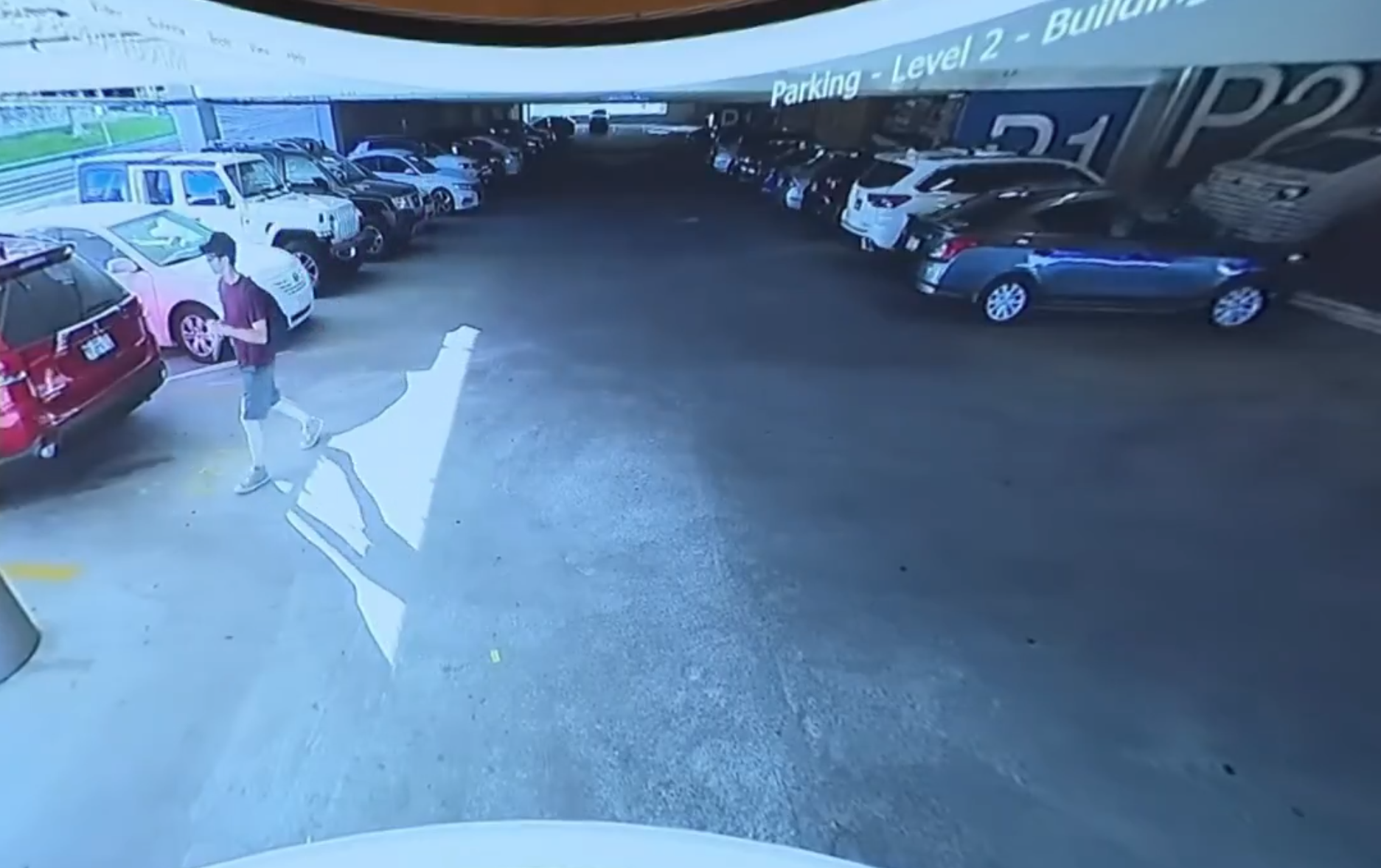 A third frame from the parking garage footage, showing a man in shorts and a cap walking through the same level of the structure