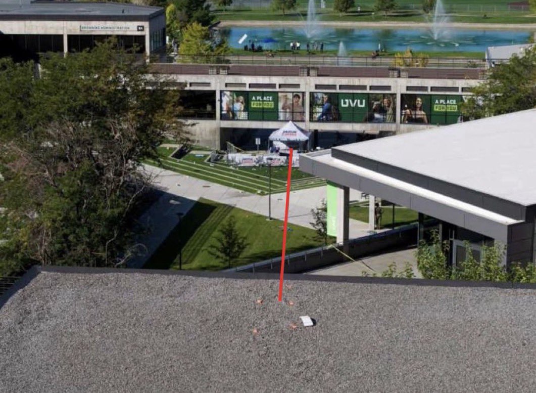Photo taken from the Losee Center rooftop, annotated with a red line marking the sightline down to the stage tent in the courtyard, with evidence markers visible on the roof surface near the vantage point