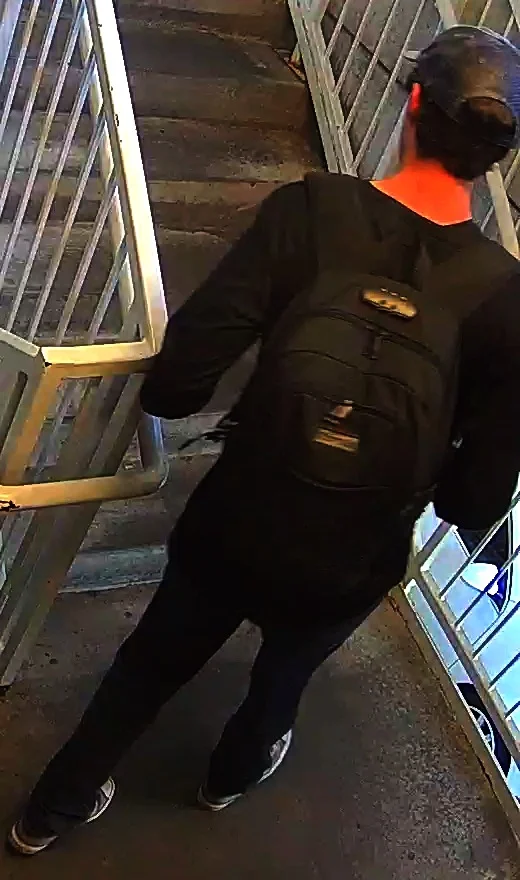 Stairwell surveillance still showing the same person of interest from behind, wearing a black backpack, descending stairs