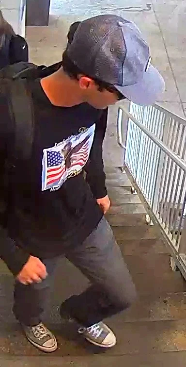 A second stairwell surveillance still showing the same person of interest from a closer angle, the American flag and eagle design visible on the shirt