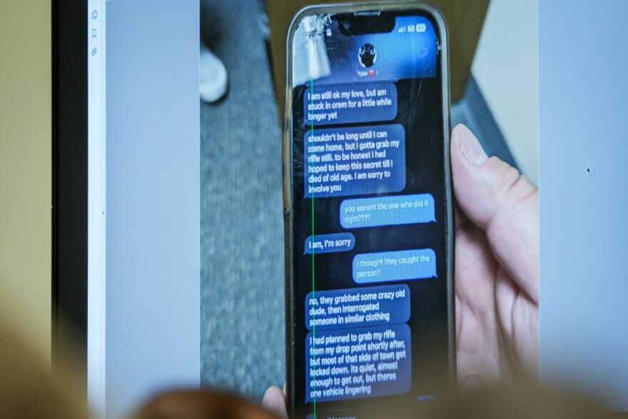 Screenshot of text messages between Tyler Robinson and Lance Twiggs displayed at the preliminary hearing, shown on a courtroom monitor